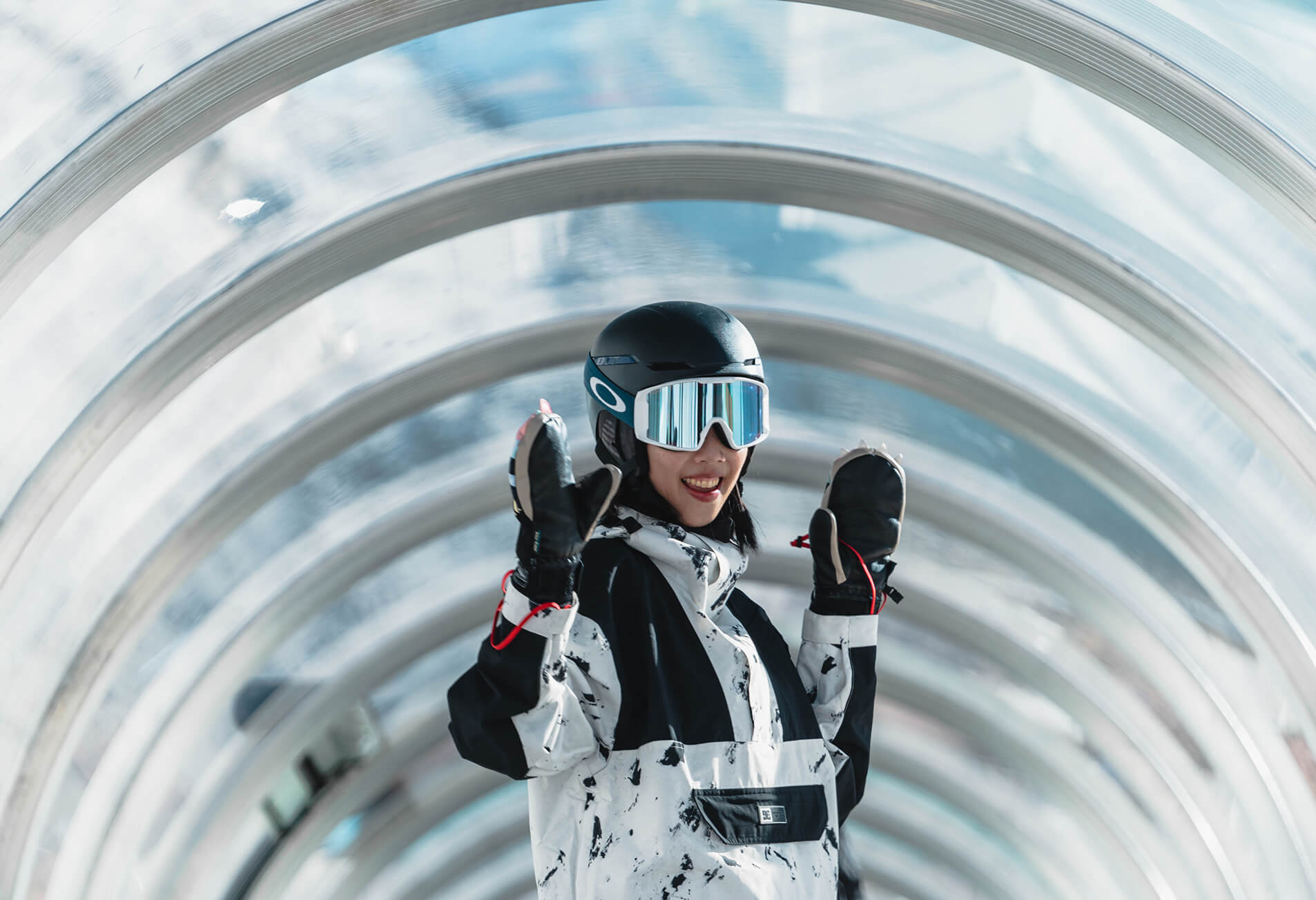 Smiling person in ski gear with helmet and reflective goggles in a transparent tunnel.