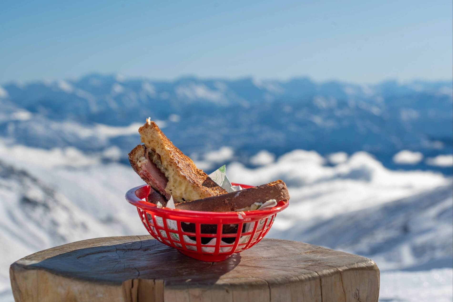 Toasted sandwich halves in a red basket on a wooden surface with snowy mountains in the background.