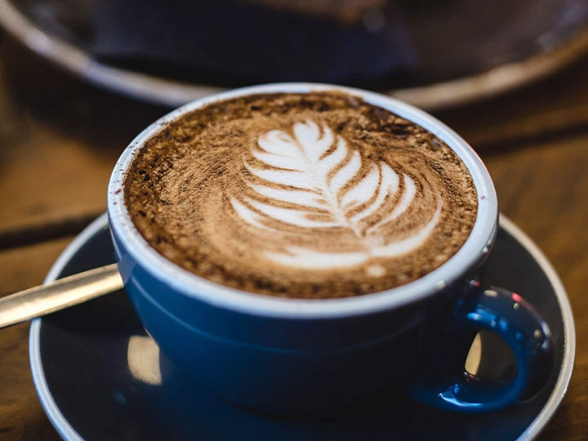 Close-up of a blue cup with latte art foam shaped like a leaf on a saucer.