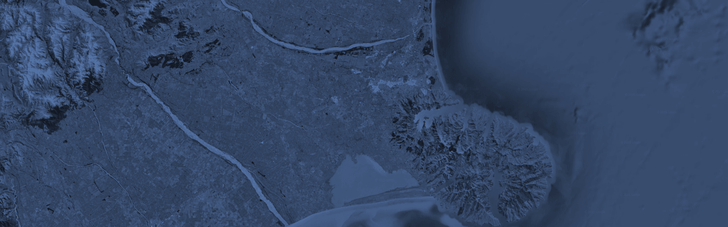 Satellite view of coastline with rivers, mountain range, and ocean area at night with blue tint.