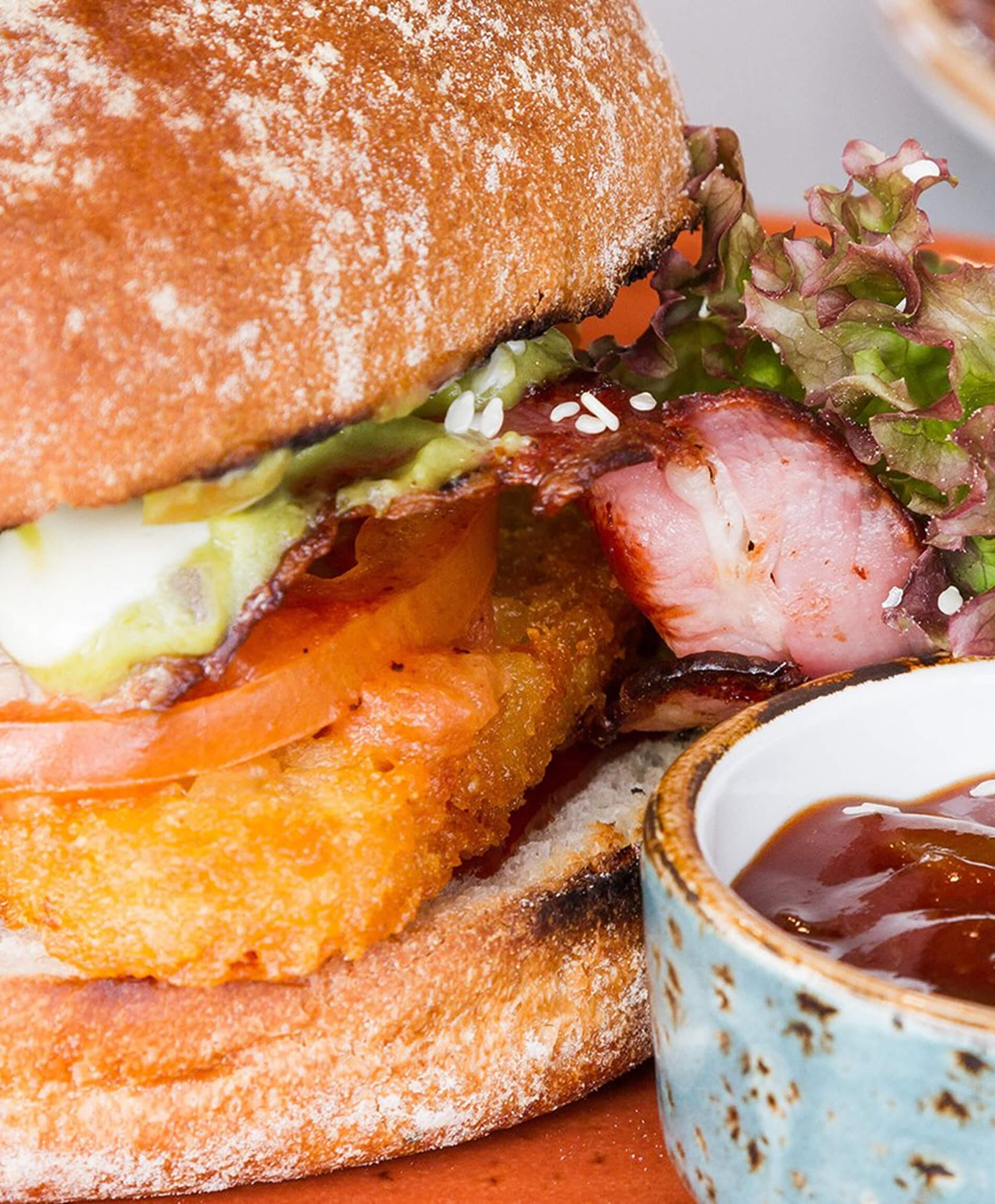 Close-up of Burger with a hashbrown, bacon, tomato, lettuce, and sauce in a ceramic bowl.