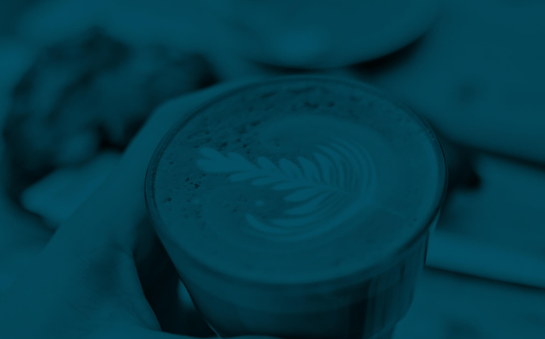 Hand holding a cup of coffee with leaf-shaped latte art on the foam.