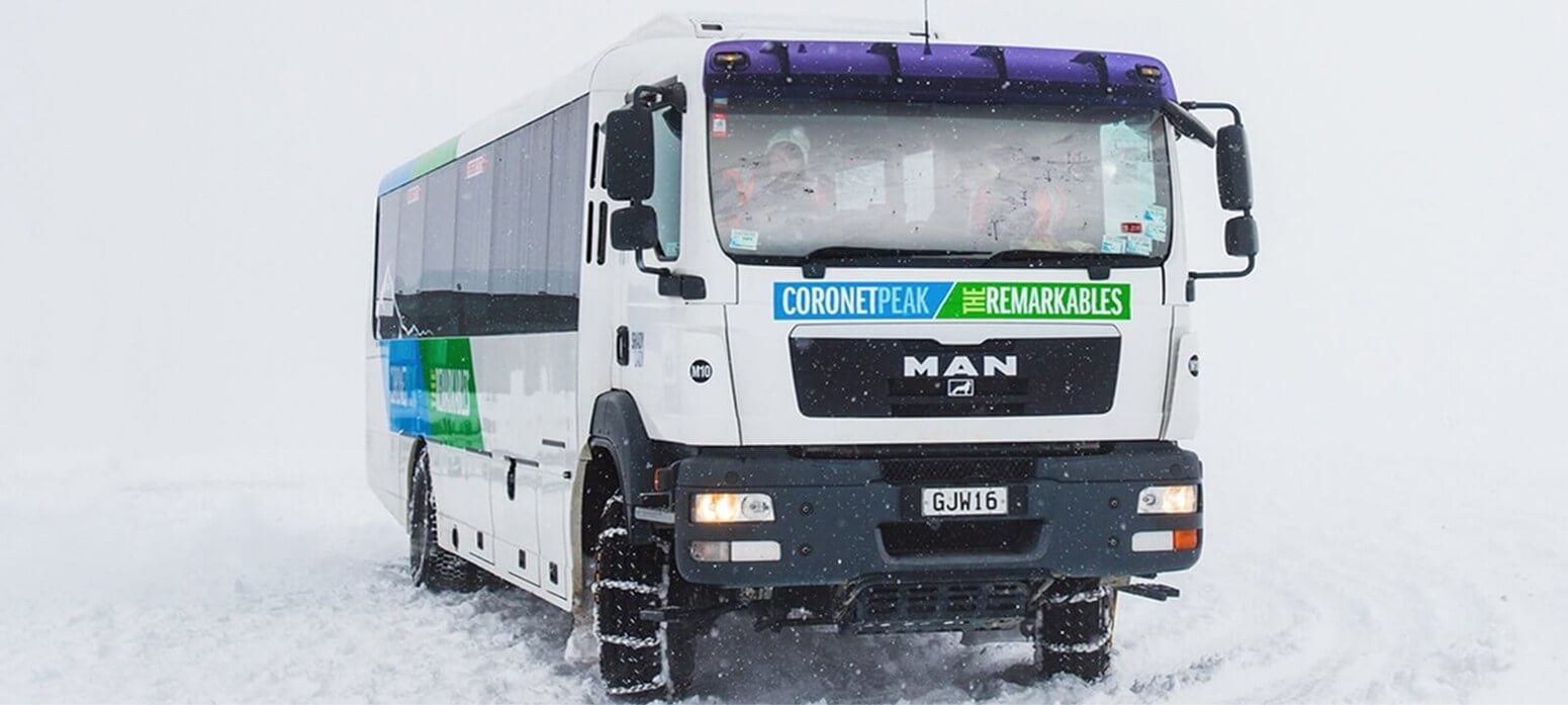 White MAN bus with coronetpeak the remarkables banner driving through snow with chains on tires.