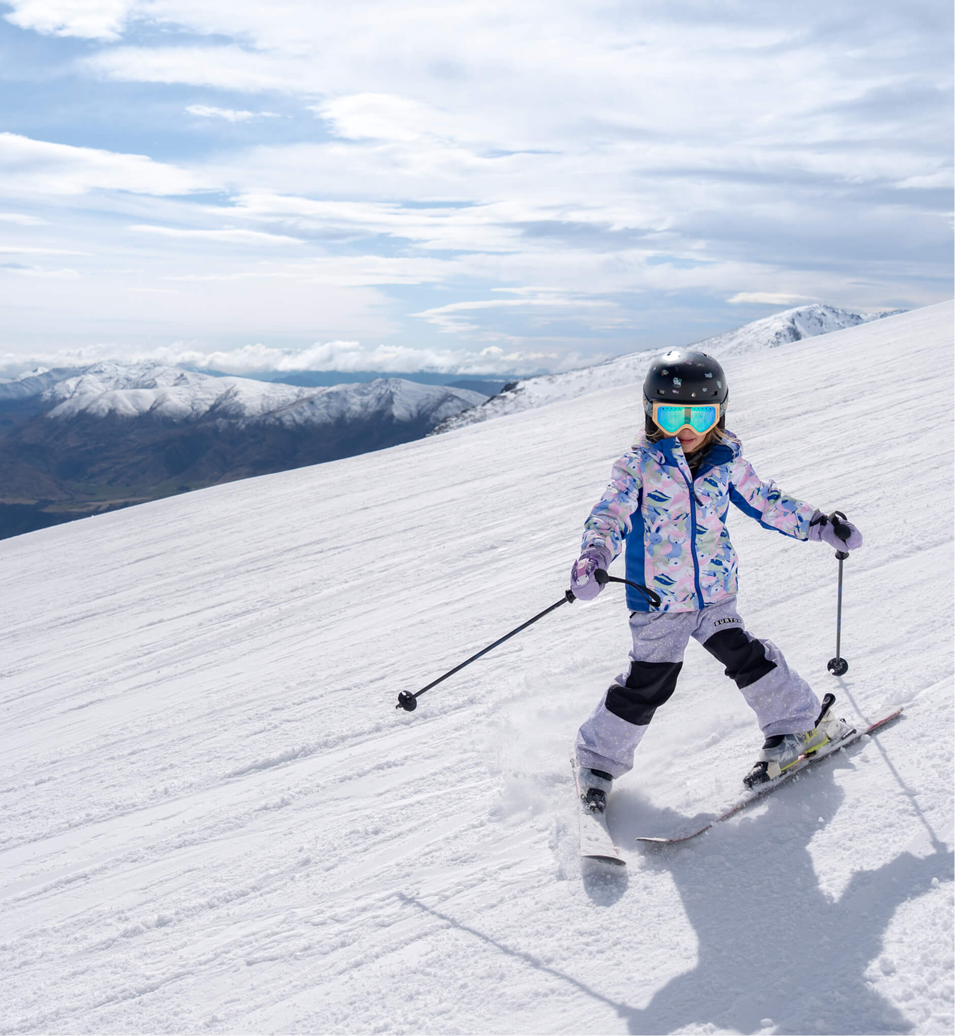 Child skiing down a snowy slope wearing a helmet, goggles, and colorful winter clothes.