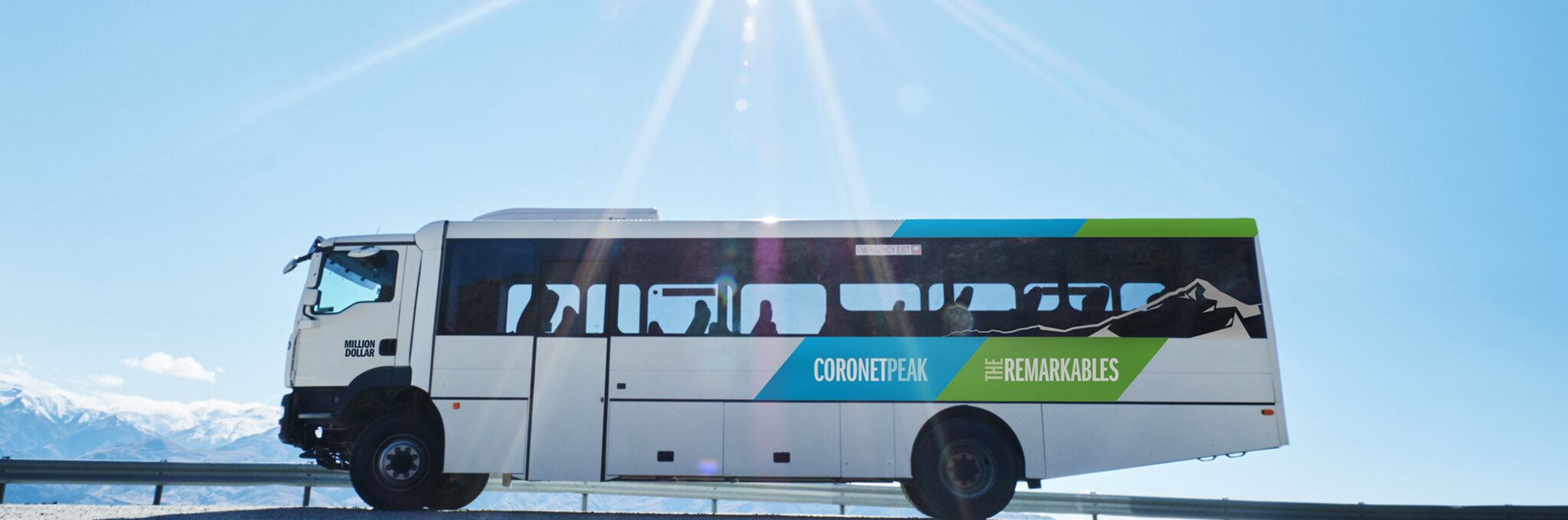 White bus with Coronet Peak The Remarkables branding parked under clear blue sky with mountains in background.