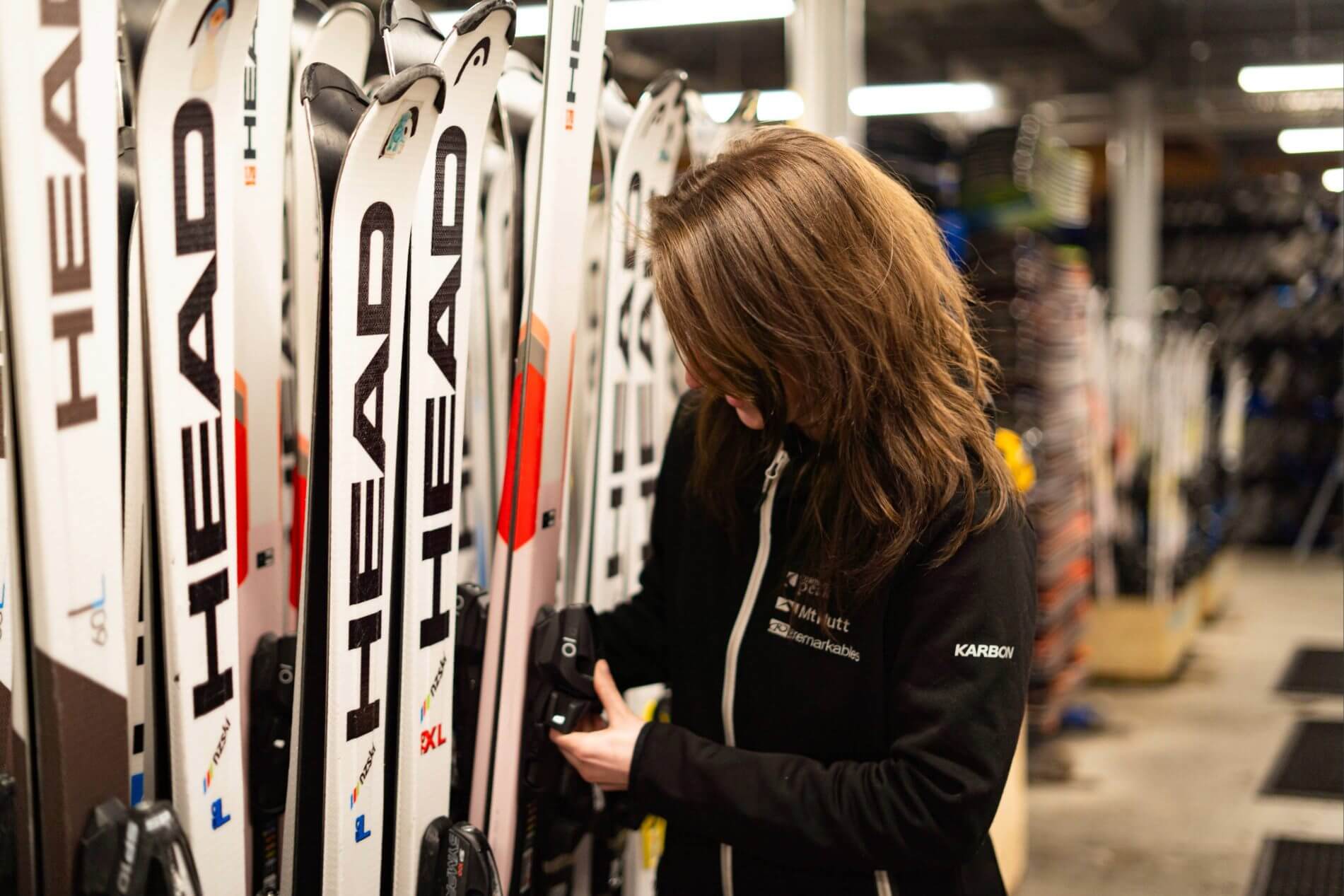 Person adjusting ski bindings on a rack of skis in a rental shop.