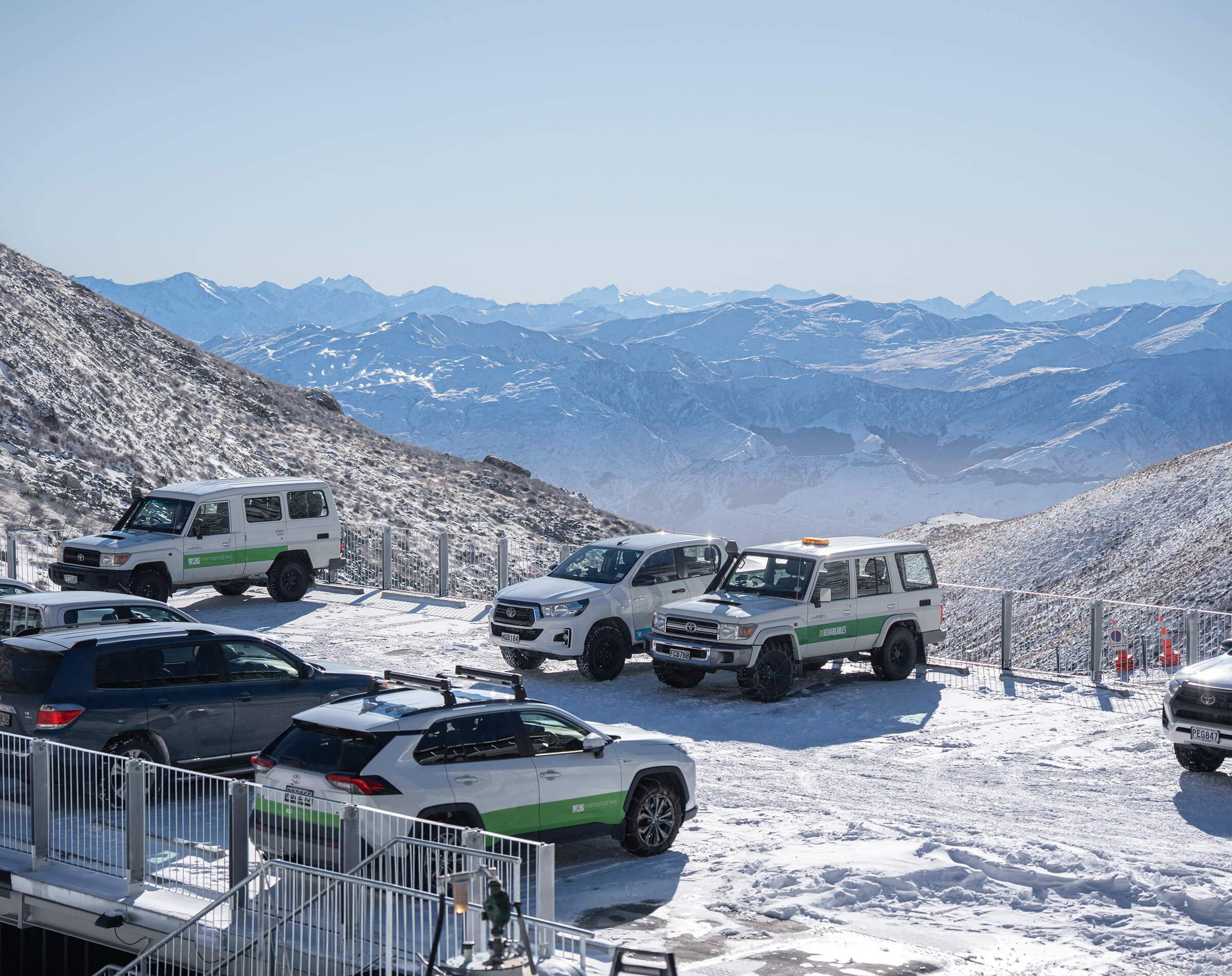 Snow-covered parking lot with several SUVs parked against a mountainous backdrop on a clear day.