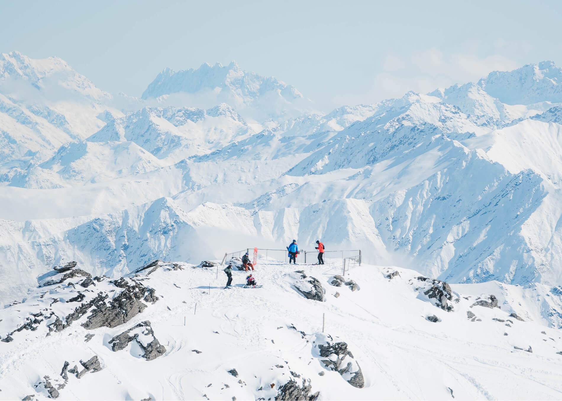 Five people on a snowy mountain peak surrounded by snow-covered mountains under a clear sky.