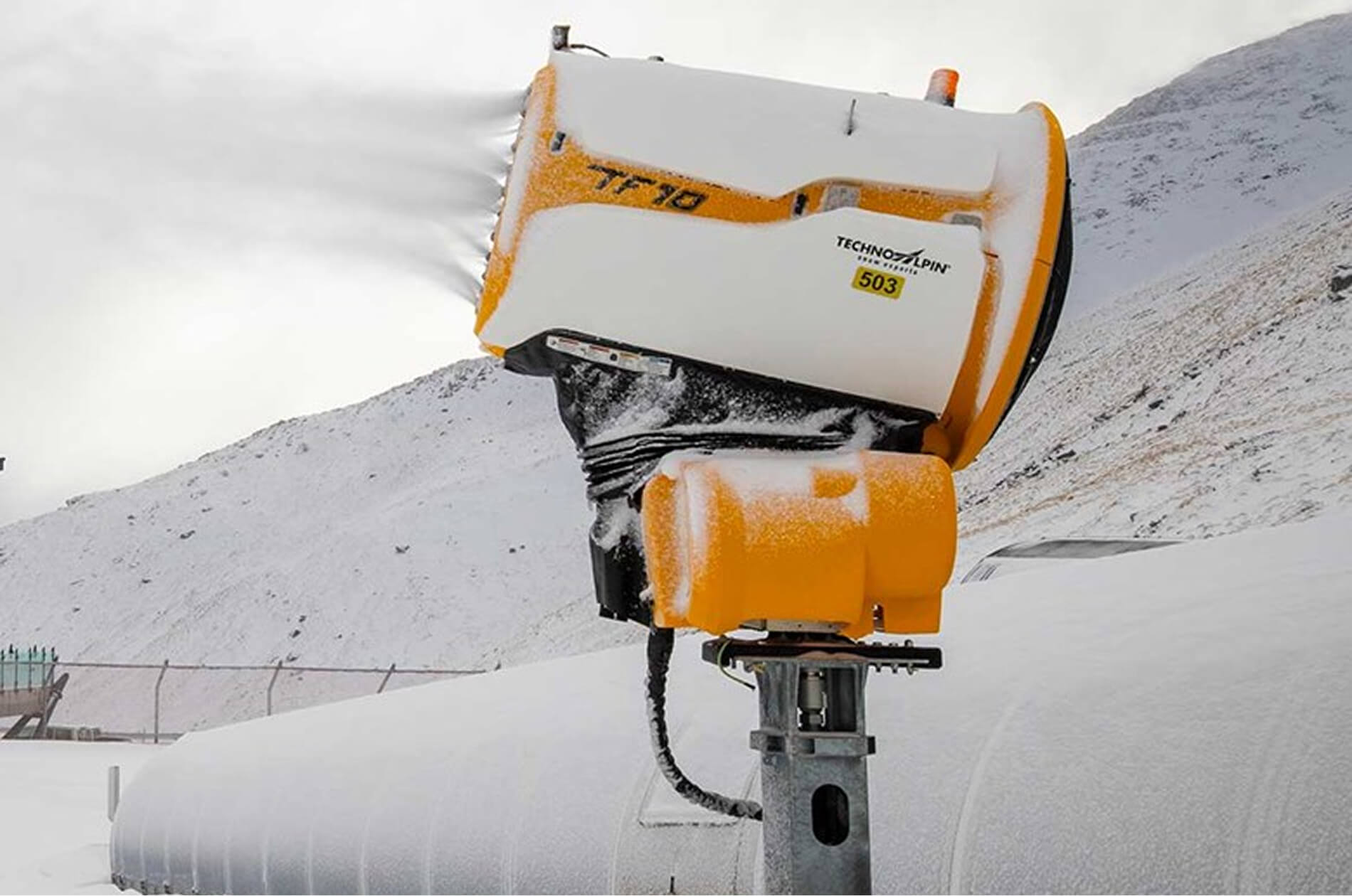 Yellow and white snowmaking machine blowing snow on a snowy mountain slope.