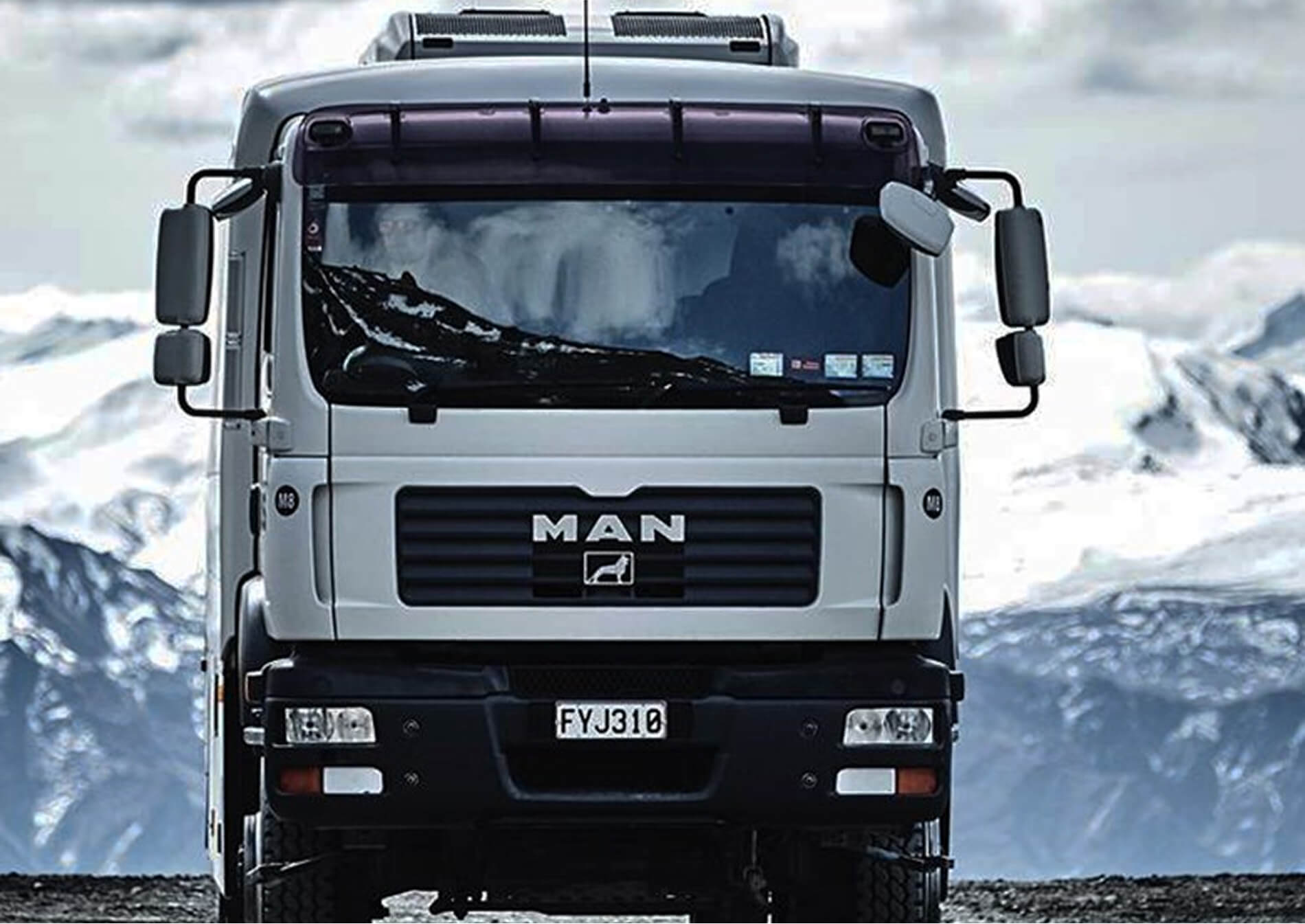 Front view of a white MAN truck with a mountain landscape reflected in the windshield.