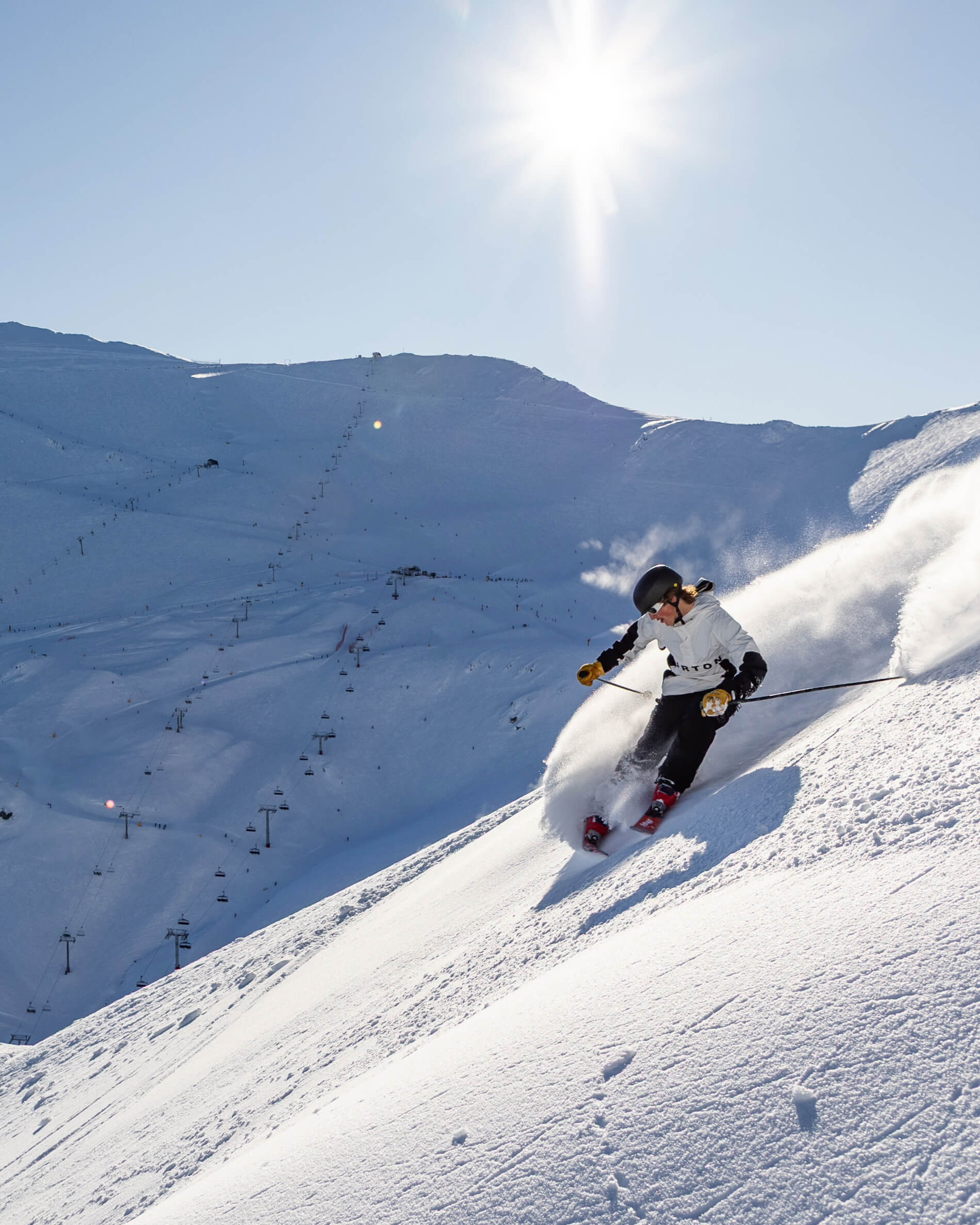 Skier wearing a helmet carving through powder snow on a bright sunny mountain slope.