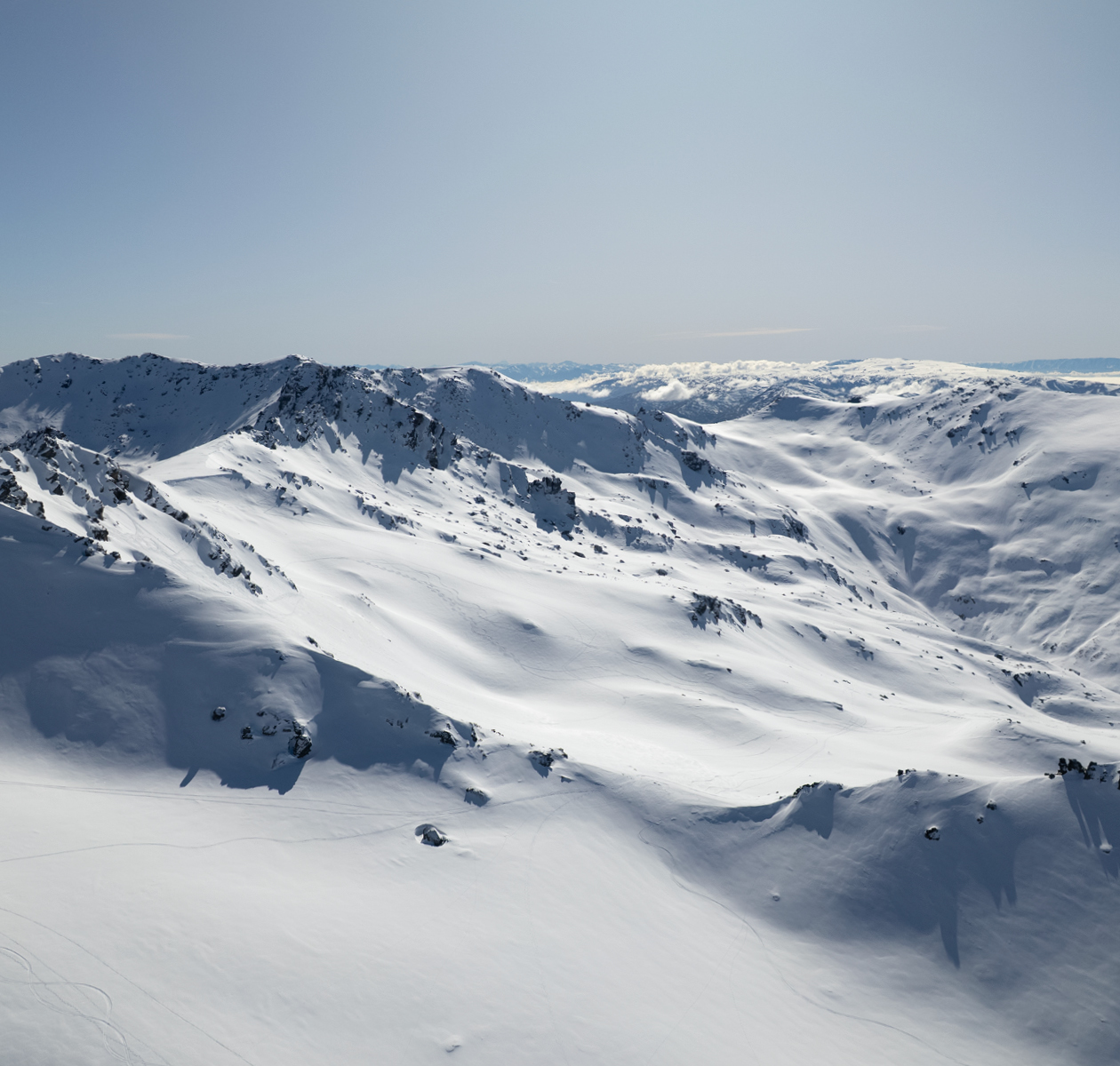 Snow-covered mountain range under a clear blue sky with rocky peaks and shadows.