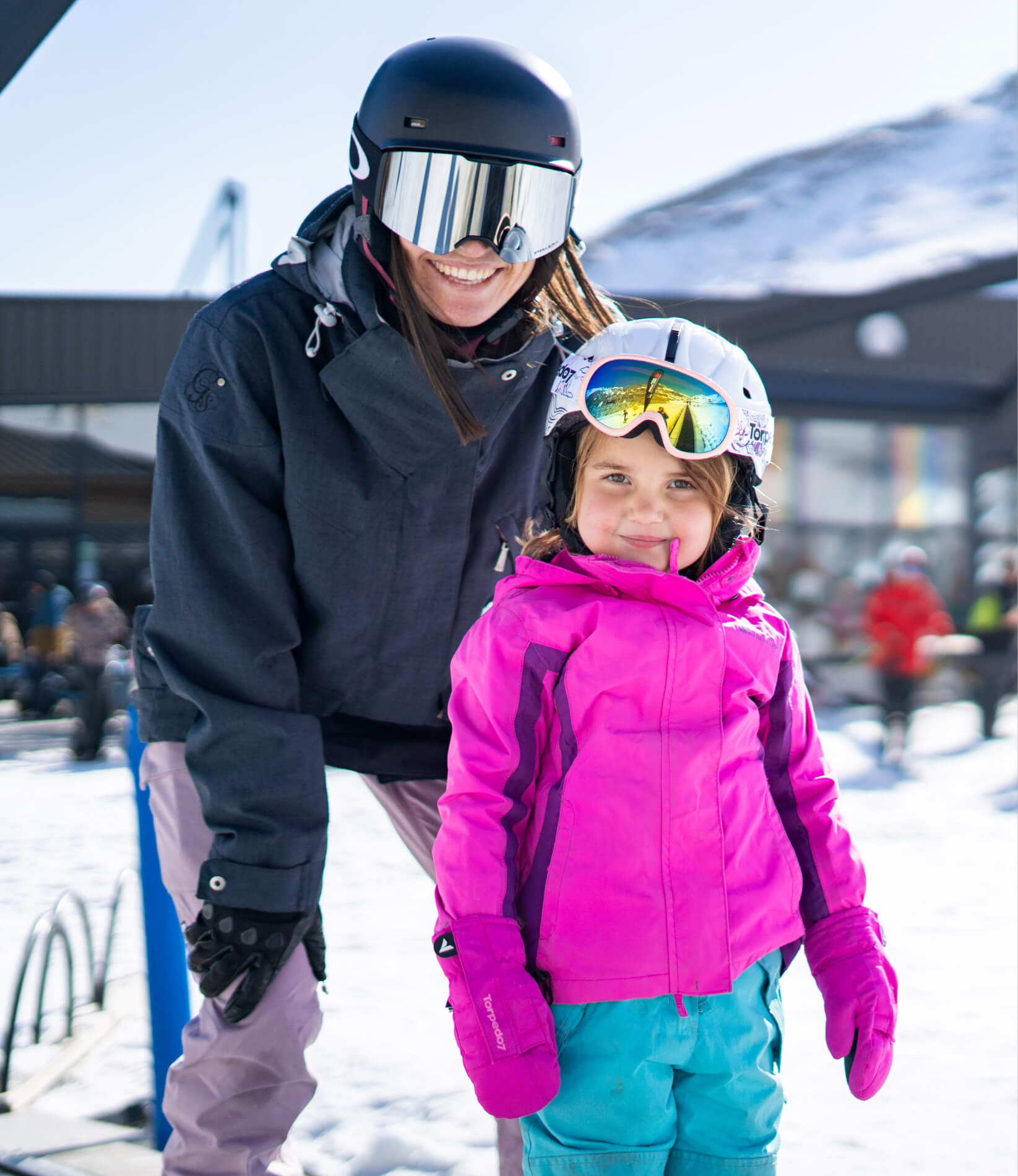 Mother and daughter smiling wearing ski helmets and goggles on a learner's ski slope.