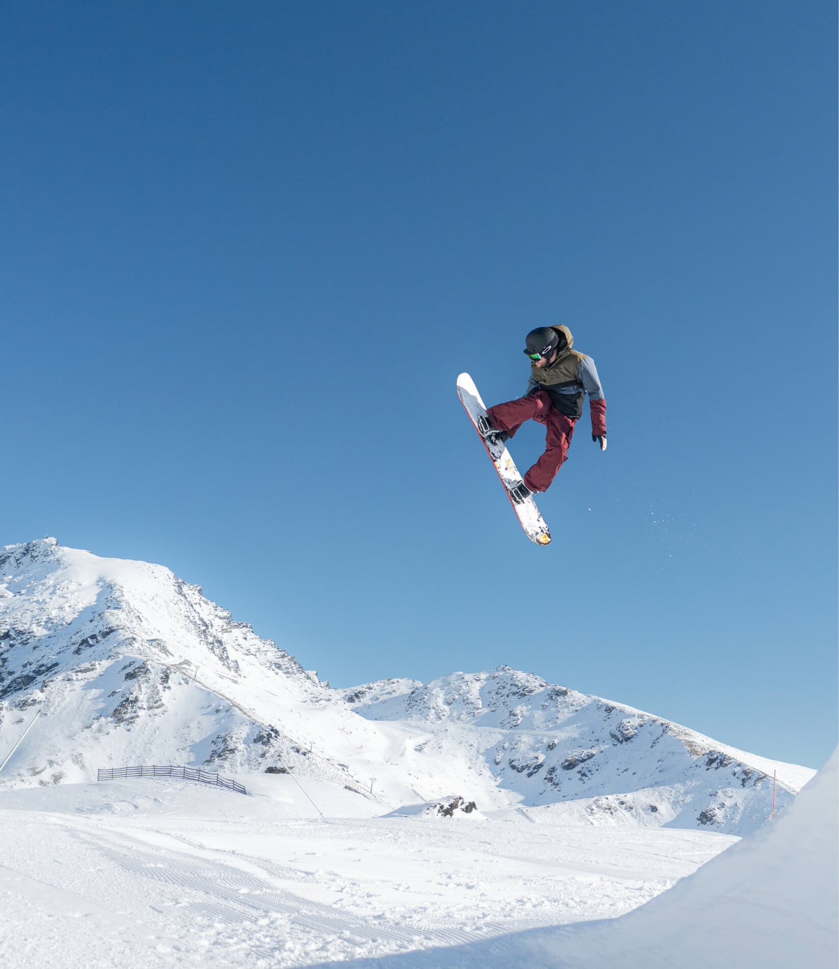 Snowboarder in mid-air performing a trick above a snowy terrain park on a sunny day.