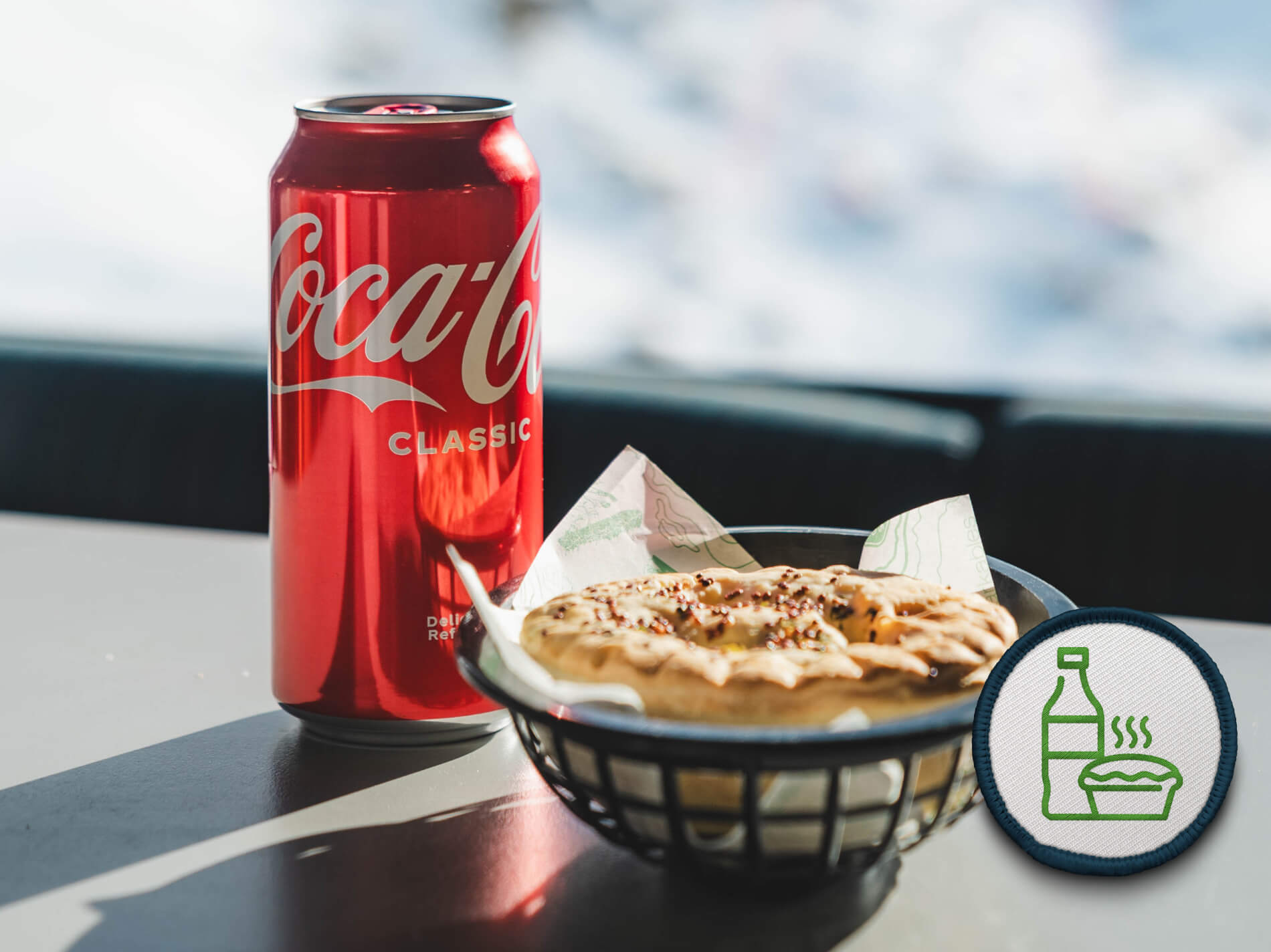 A red Coca-Cola Classic can next to a black basket holding a pie.
