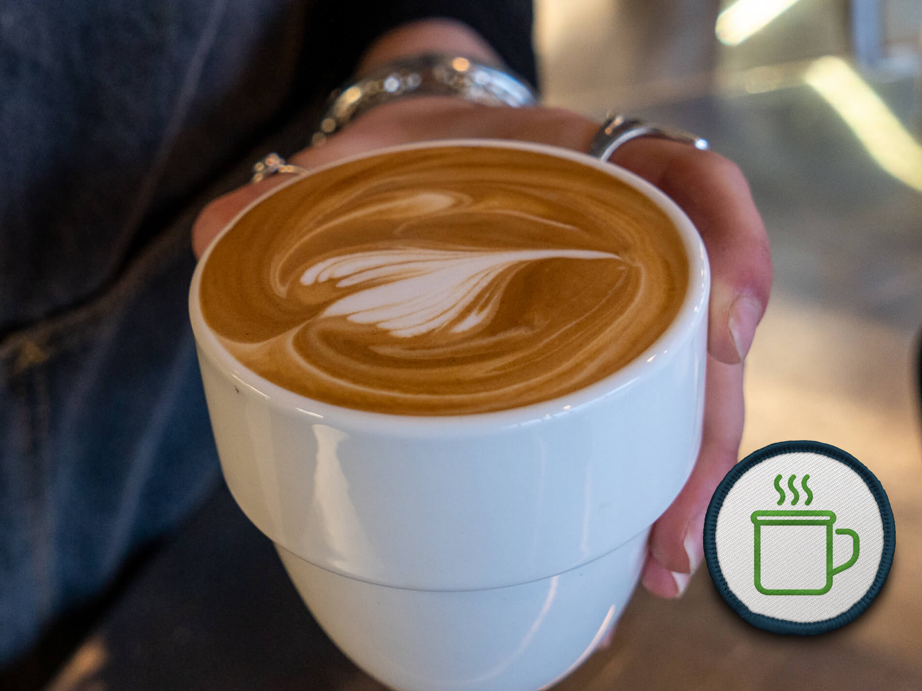 Hand holding white cup of coffee with latte art.